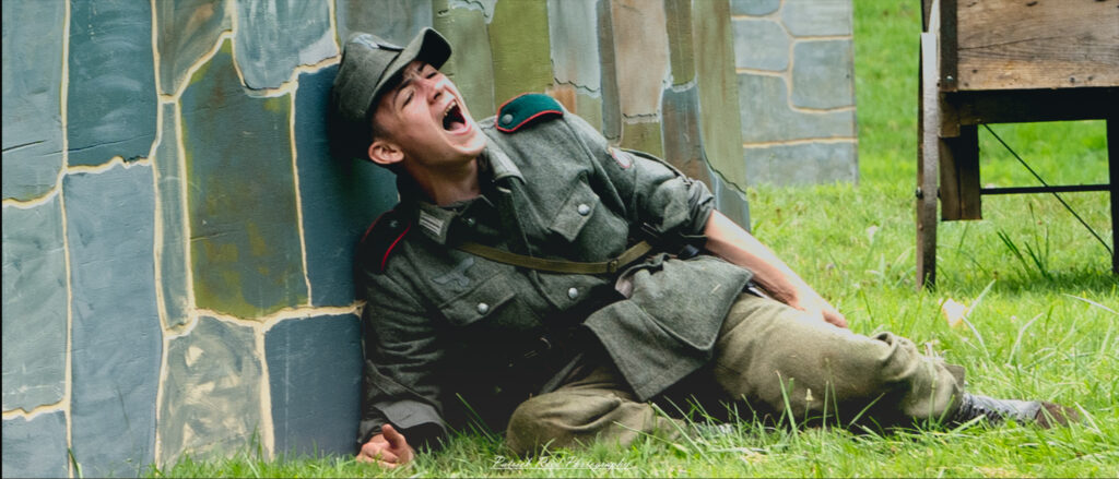 A soldier hidden behind a wall, his face contorted in a scream as he shouts out, either in communication or in response to the chaos around him. The scene captures a moment of intense emotion and urgency, set against the backdrop of a tense battlefield.